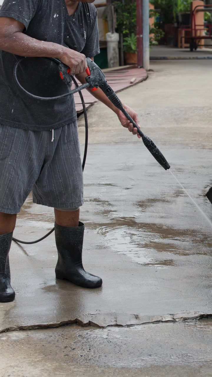 Um homem de botas usa uma mangueira de água de alta pressão para limpar concreto na Tailândia.