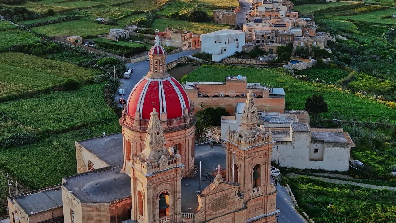 Chiesa a Malta con cupola rossa circondata da campi verdi e strade