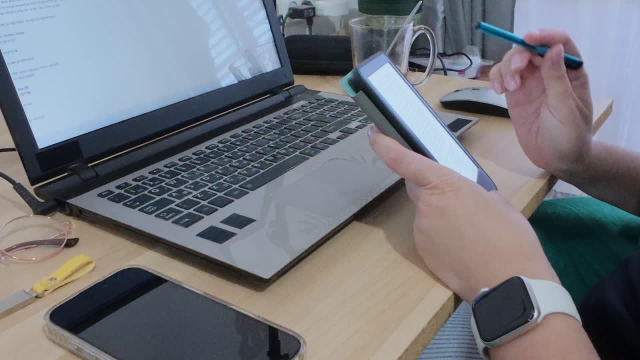 Modern portable office setup with hands using a tablet, alongside a laptop and other essentials