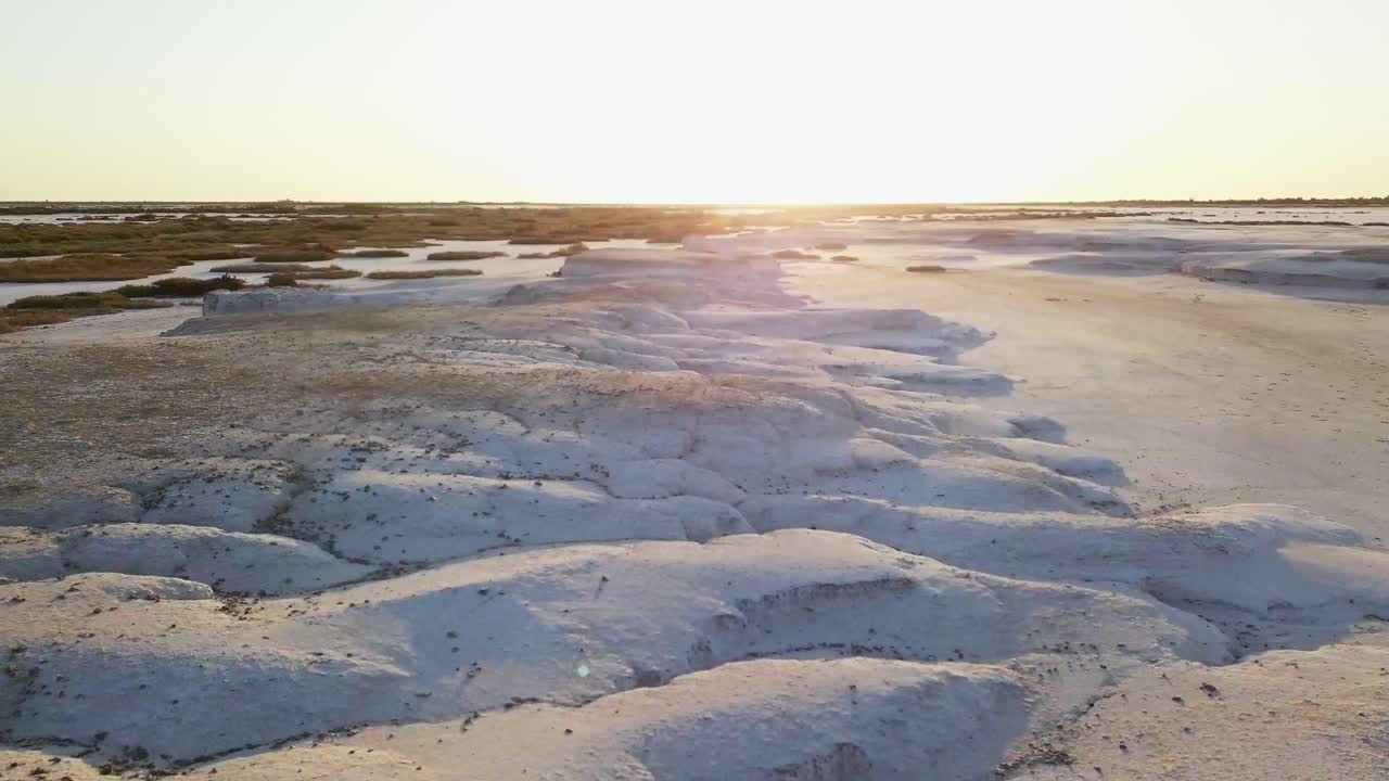 vista aérea en movimiento de un campo de sal, un campo nevado con poca vegetación y un cielo al atardecer