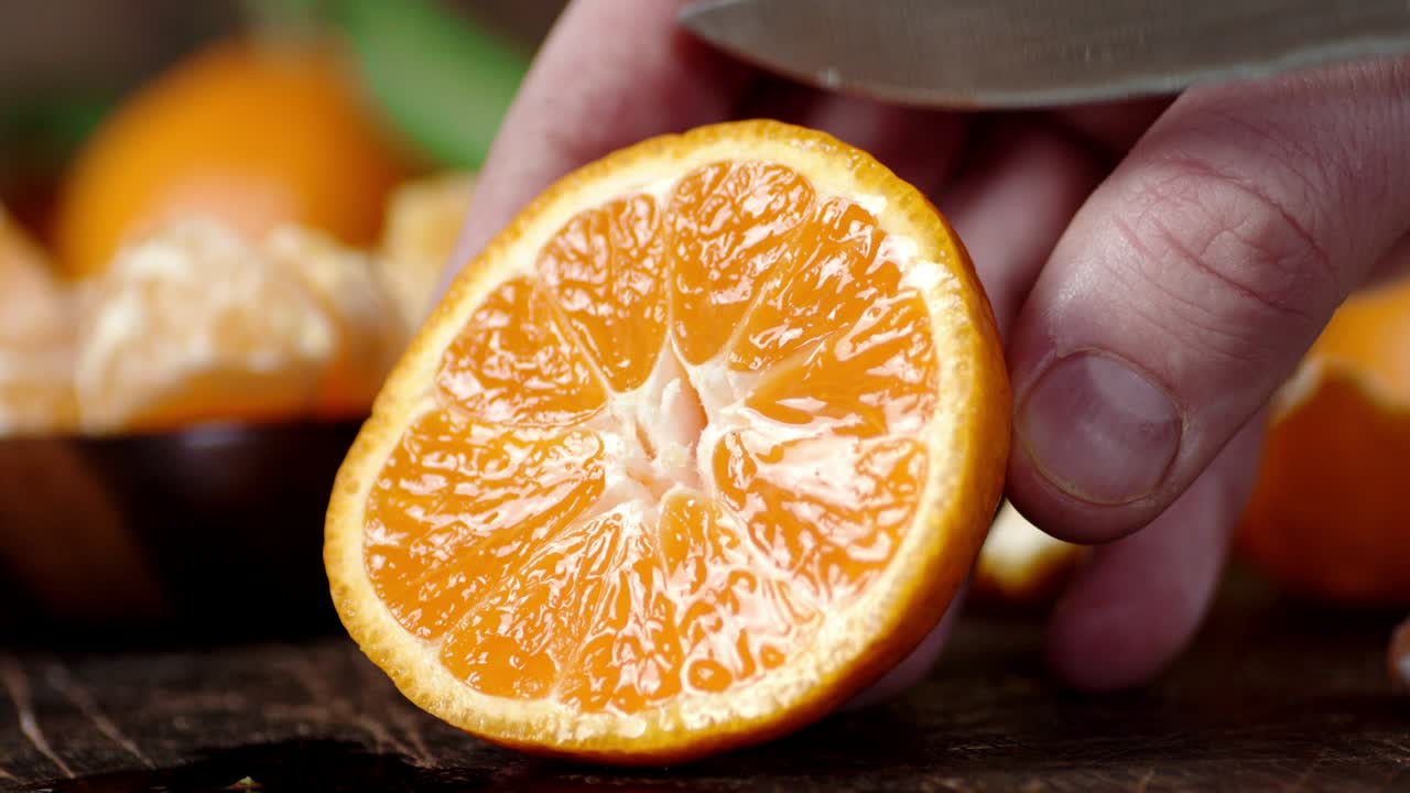 las manos de los hombres con un cuchillo exprimen el jugo de la mandarina madura.