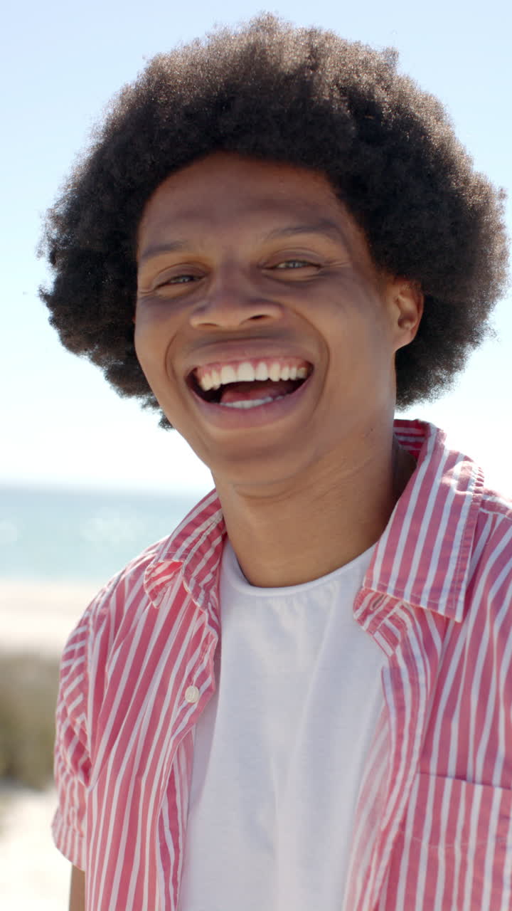 Vertical video: Smiling man enjoying sunny day at beach, wearing striped shirt