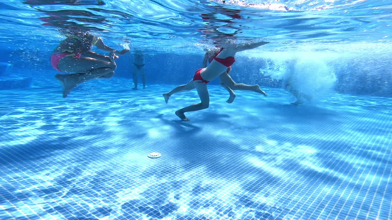 Female legs under water in the pool. Children are walking in the clear blue water of the swimming pool. Underwater camera shoot the video from the bottom of the pool.