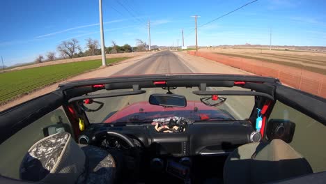 people in suv with open roof driving on road along fields - arizona