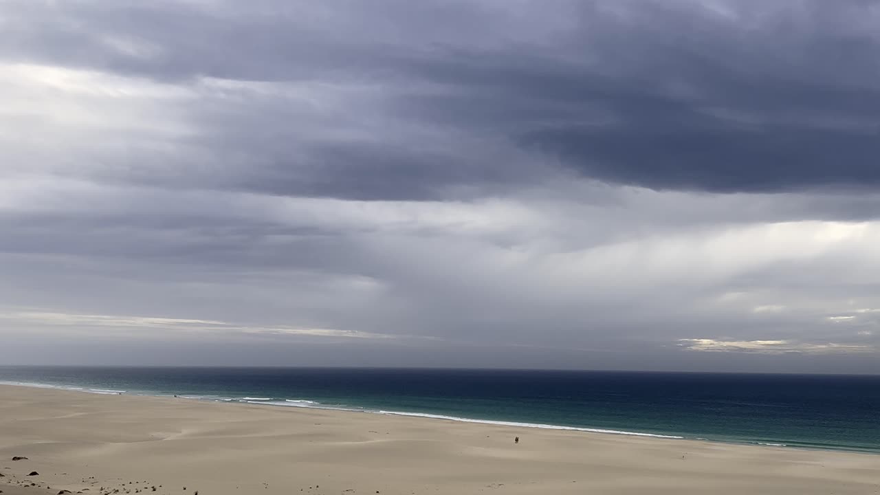 Praia de Chaves Beach featuring two distant people on empty sandy shoreline, calm ocean, and dramatic overcast skies, capturing the beauty of nature before a storm, people in the distance