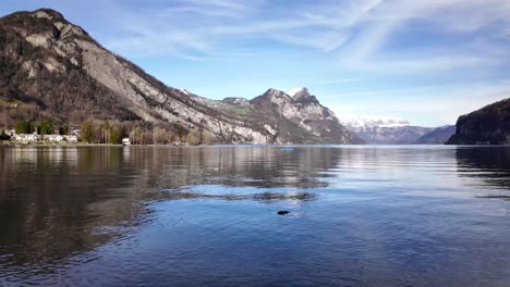 Idyllic-timelaps-of-Walensee,-tranquil-Lake-in-Switzerland,-small-village-Quinten-and-Weesen-featuring-peaceful-water-surrounded-by-Churfirsten-mountain-range-with-snow-covered-Swiss-alps-at-distance