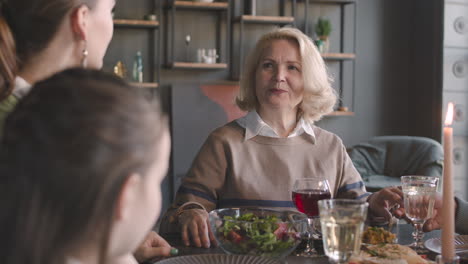 senior woman talking with her family while sitting at dinner table and having meal at home