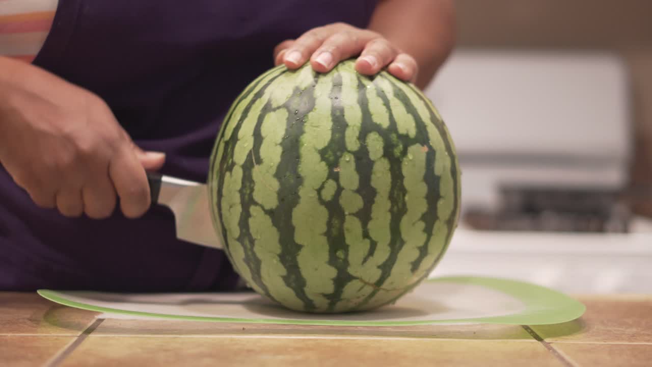 Woman carefully slicing a whole watermelon in half, CLOSE UP