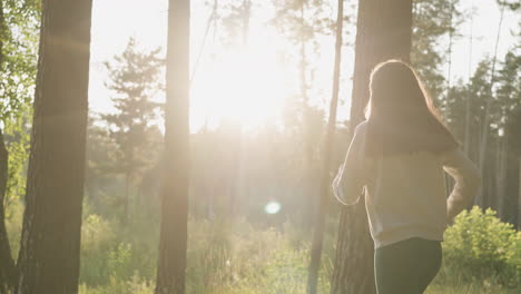 a woman walks through a forest with sunlight shining through the trees