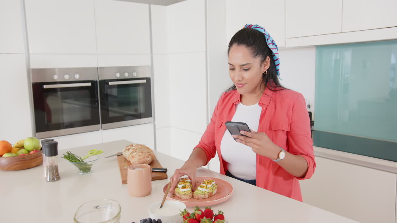 Eating healthy breakfast, asian woman holding smartphone in modern kitchen, at home
