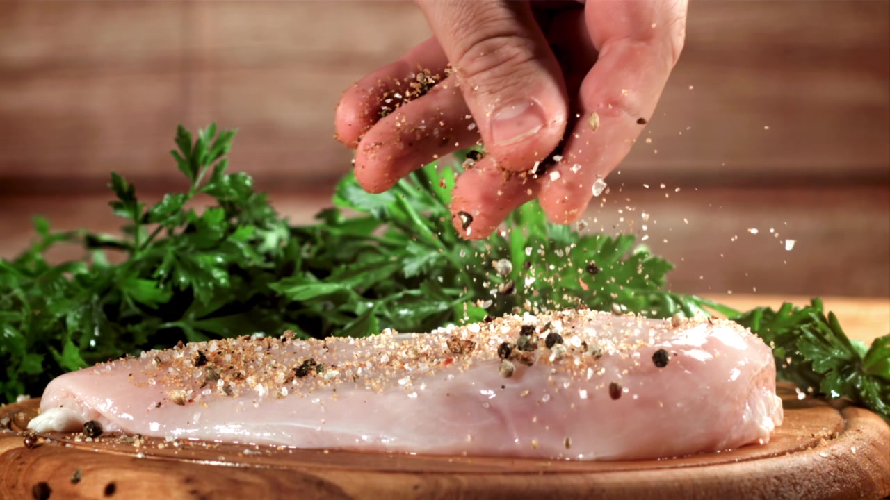 Hand streut Gewürze auf rohes Hähnchen