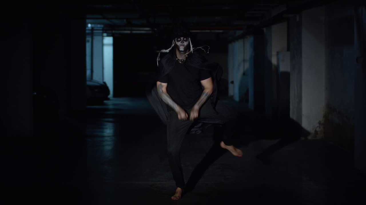 Uomo pazzo e spaventoso con trucco da scheletro di Halloween che balla in un corridoio buio del parcheggio al rallentatore.