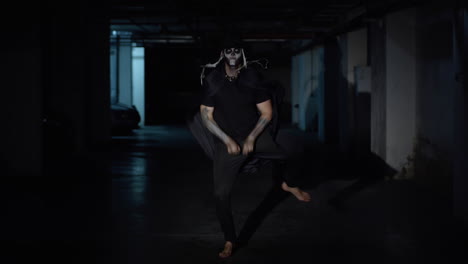 Crazy-scary-man-with-skeleton-Halloween-makeup-dancing-against-dark-parking-hallway-in-slow-motion