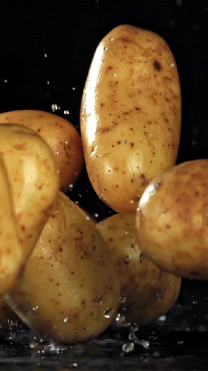 Patate crude che cadono nell'acqua con schizzi su sfondo nero