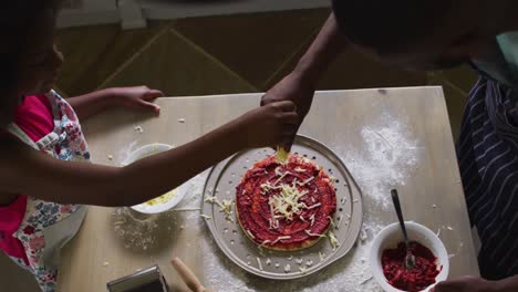 sección media de la hija afroamericana y su padre haciendo pizza juntos en la cocina