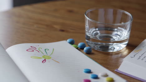 open notebook with water glass and pills on wooden table