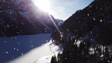 Frozen-lake-water-covered-in-snow-near-majestic-mountain-ranges,-aerial-drone-view
