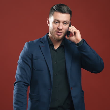 happy businessman talking the phone. handsome man in suit holding folder and speaking on the phone in studio. office manager on dark red background.