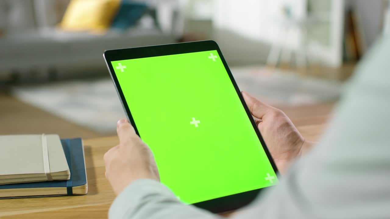 hombre usando pantalla de maqueta verde computadora tableta digital en modo retrato mientras está sentado en su escritorio. en el fondo acogedora sala de estar.