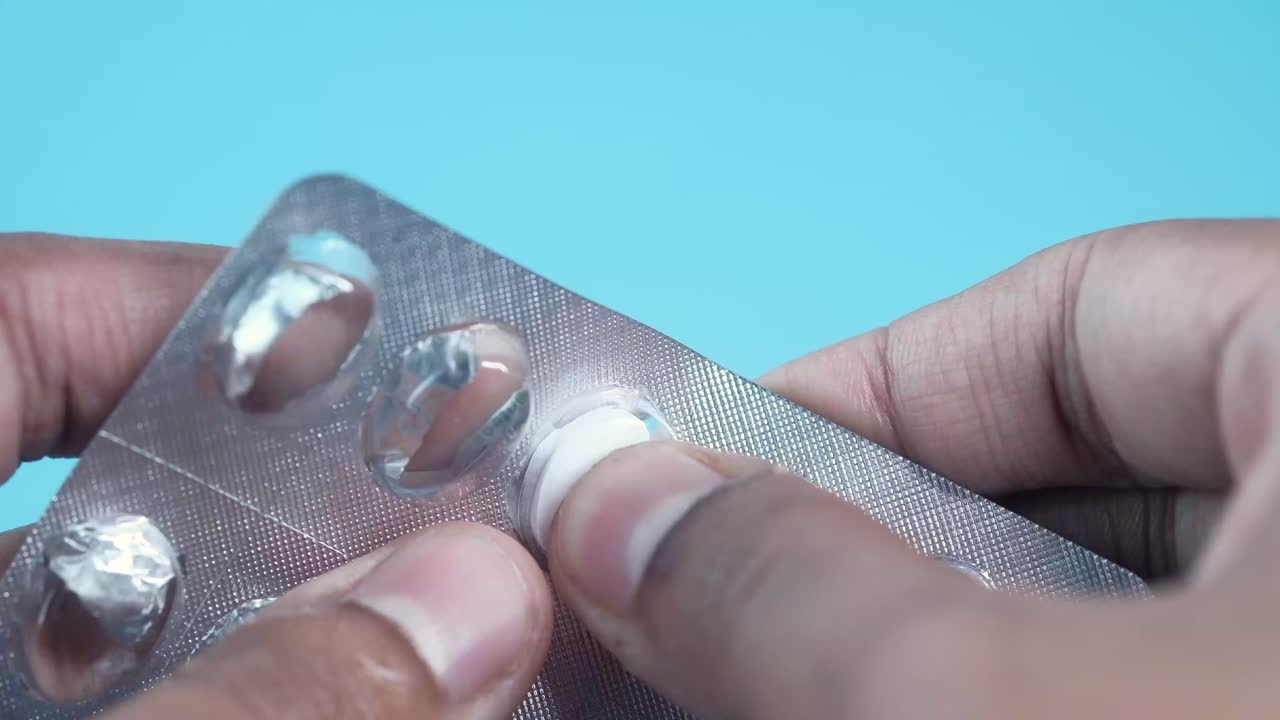 pessoa a tomar uma pílula oval branca de uma embalagem blister