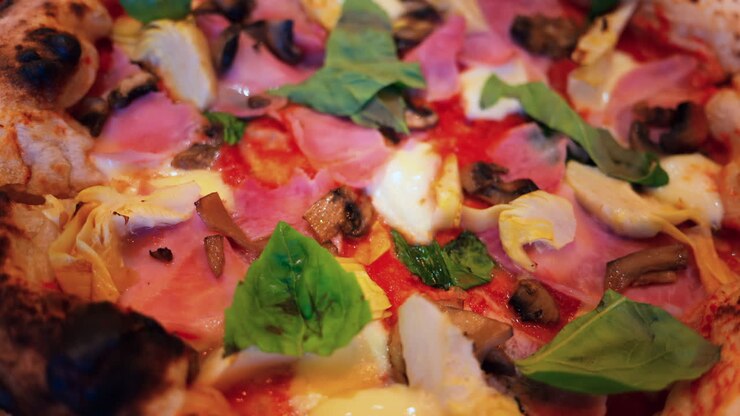 Primo piano di una pizza con carciofi, prosciutto, funghi e basilico
