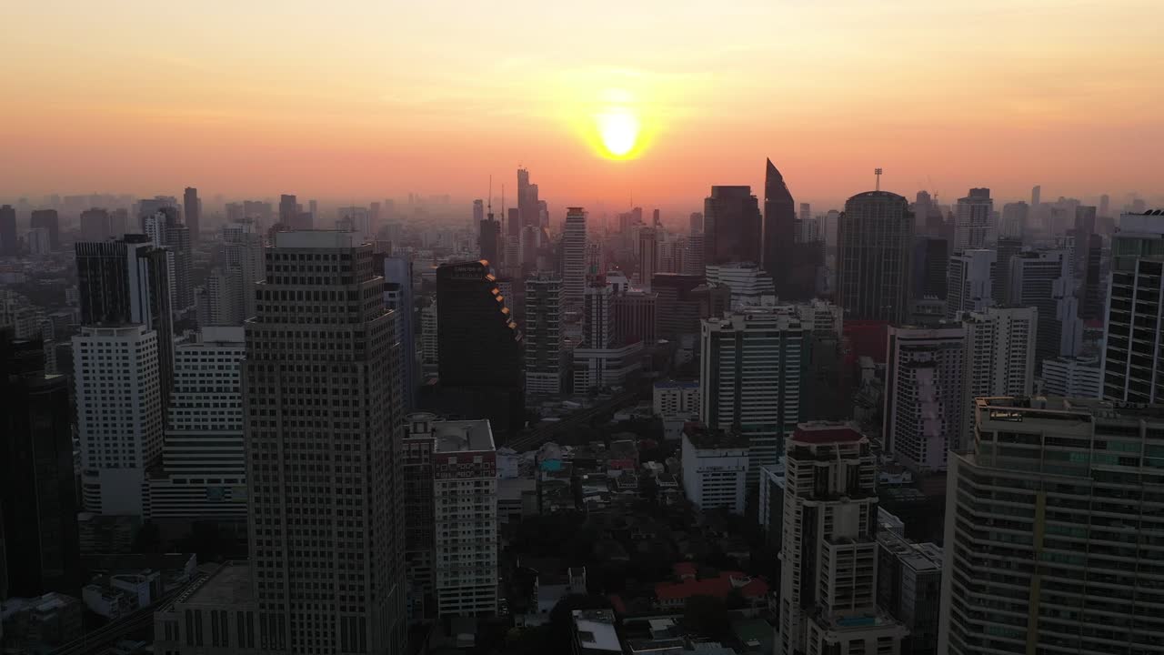 Epic aerial drone rising above buildings, skyline and skyscrapers of Sukhumvit district during colorful red sunset in Bangkok, Thailand.