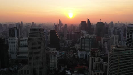 epic aerial drone rising above buildings, skyline and skyscrapers of sukhumvit district during colorful red sunset in bangkok, thailand.