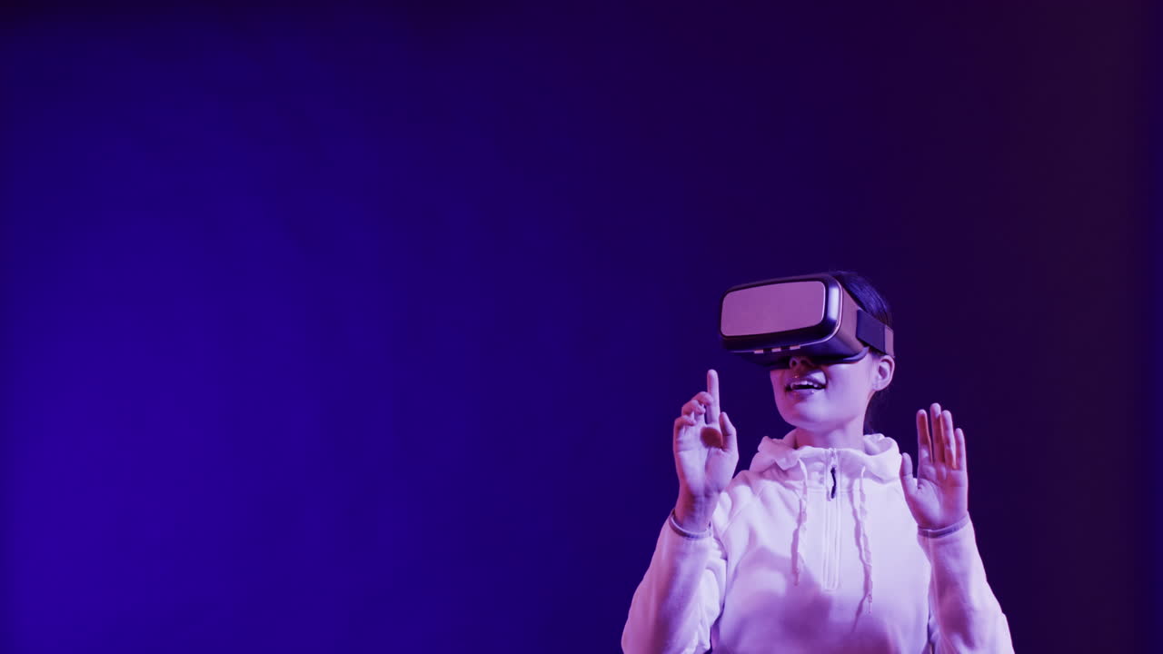 Asian woman using vr headset, touching virtual screen on blue background, copy space, slow motion