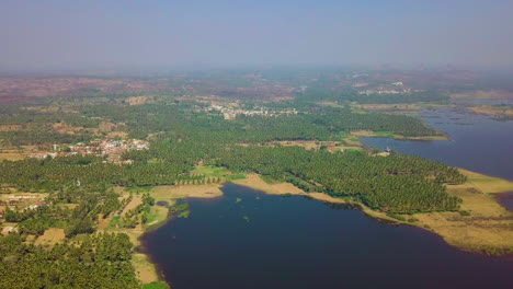 wide angle shot of ramanagara lake surrounded in greenery and an isolated town in karnataka, india during daytime. drone view.