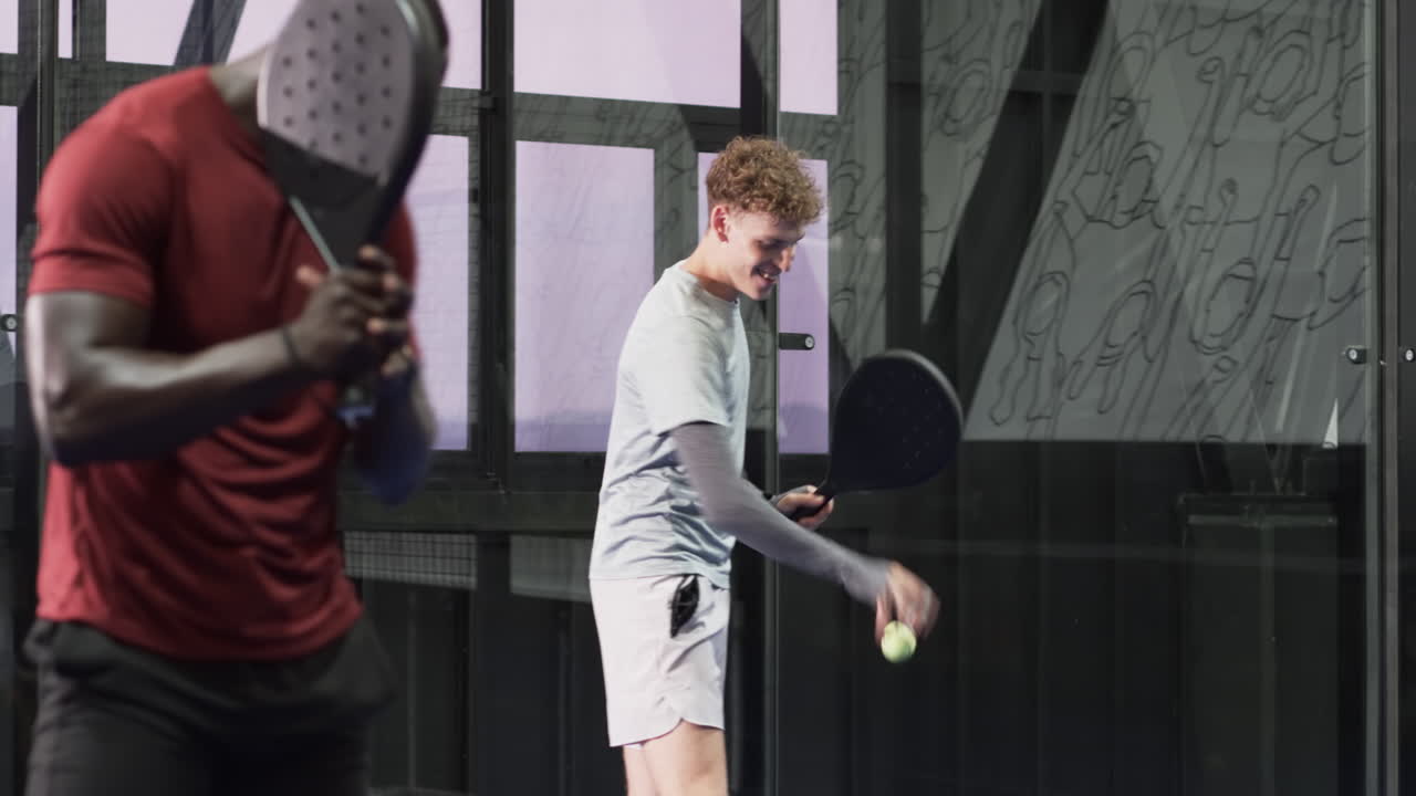 Young man holding padel racket, smiling confidently on indoor court