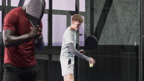 young man holding padel racket, smiling confidently on indoor court