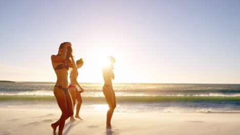 Young-women-running-into-ocean-at-sunset-in-slow-motion-girls-taking-off-clothes-on-tropical-beach