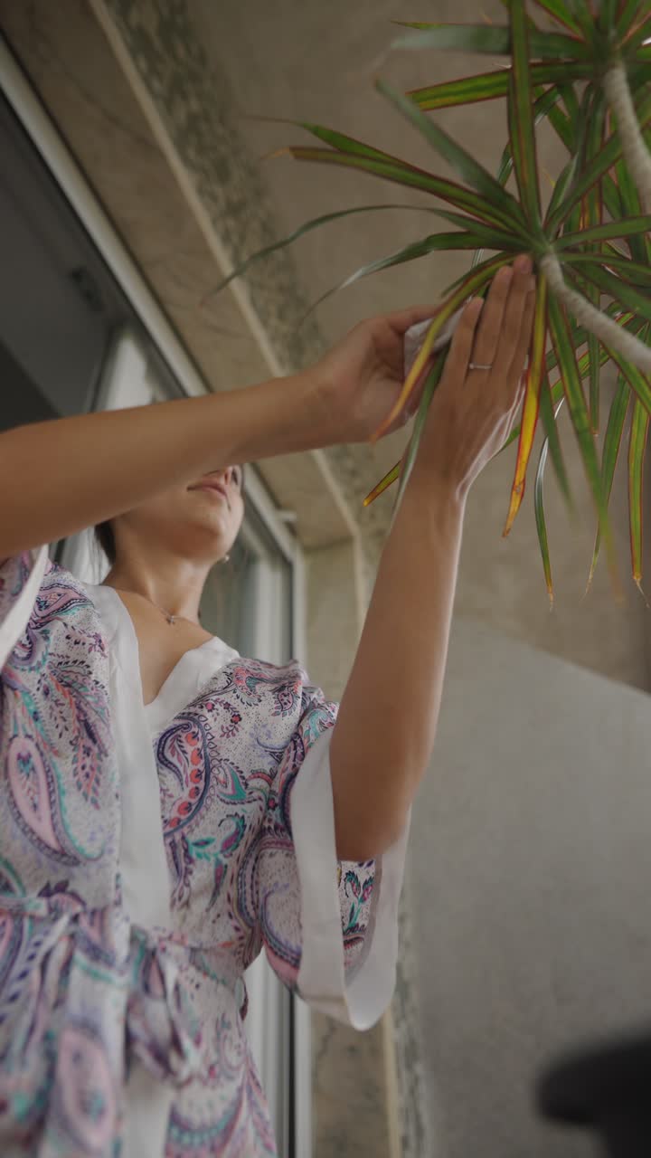 Woman Cleaning a Plant on a Balcony