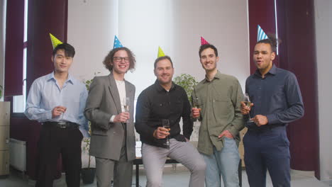 Happy-Multiethnic-Group-Of-Male-Colleagues-Holding-Champagne-Glass,-Posing-And-Looking-At-The-Camera-At-The-Office-Party