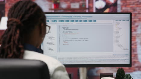 Woman in home office looking at UI on PC screen, typing code