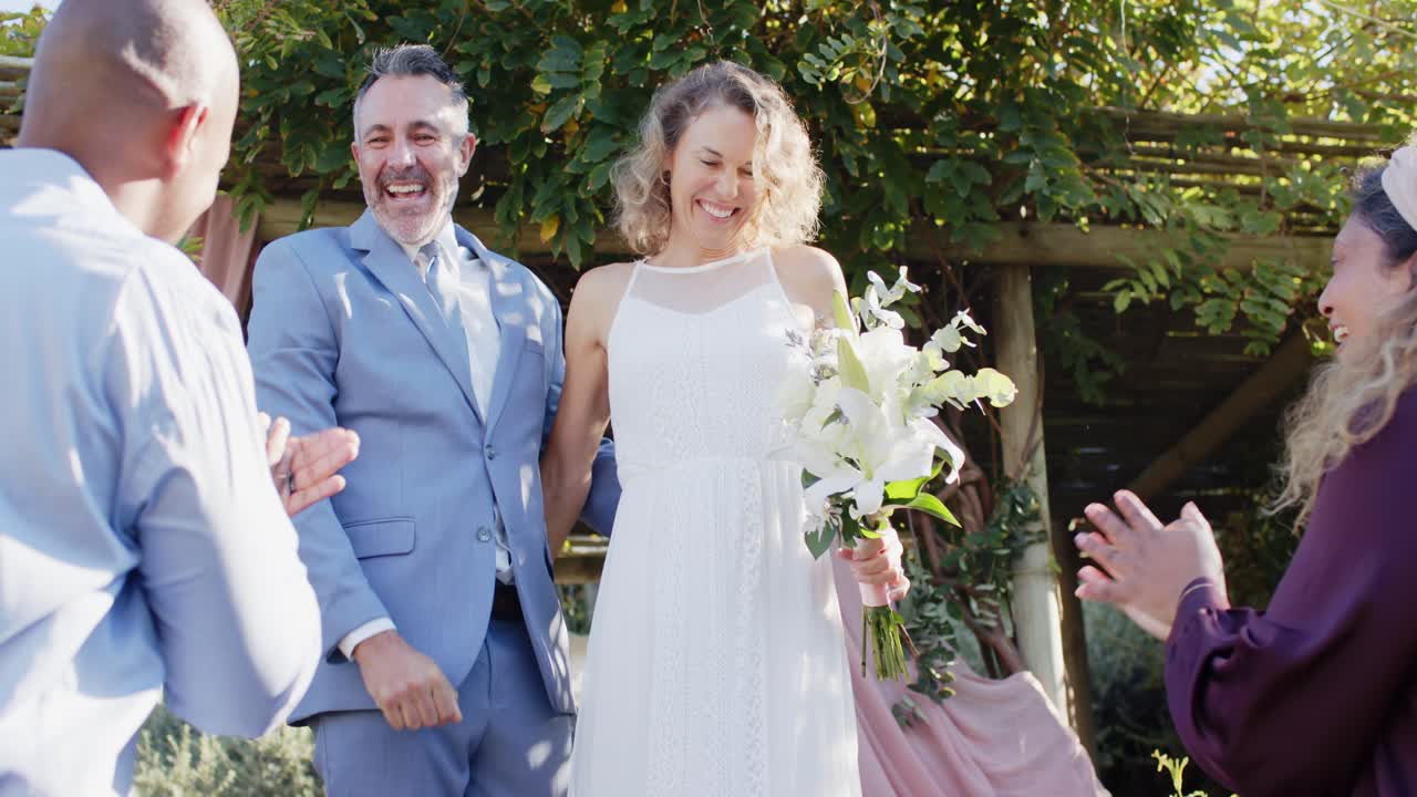Sposi novelli che festeggiano dopo le promesse nuziali, lo sposo stringe la mano a un invitato, la sposa offre il bouquet e abbraccia un invitato sotto l'arco.
