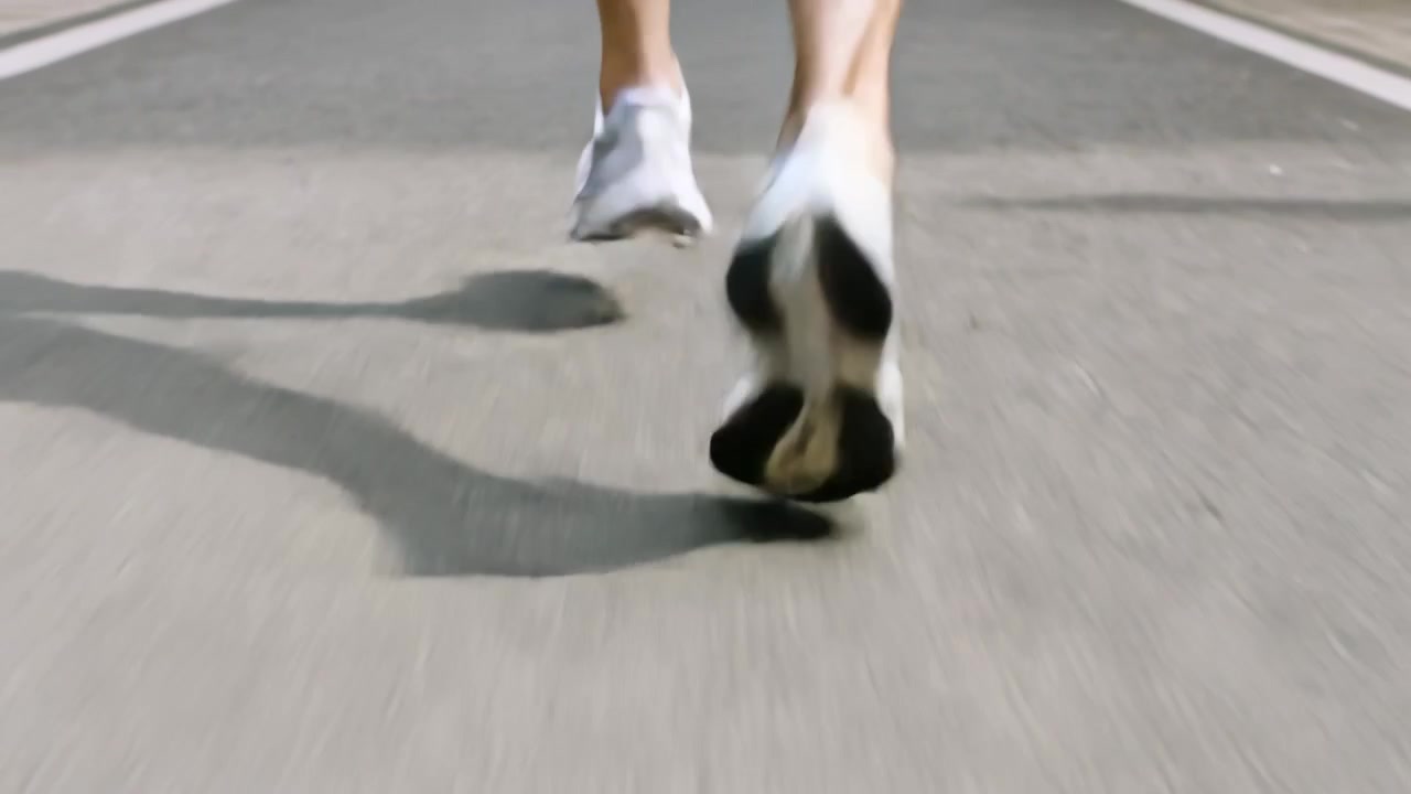 İtişle birlikte, koşucunun alt bacakları ve ayakları fitness için asfalt yolda sallanıyor, beyaz ayakkabılar