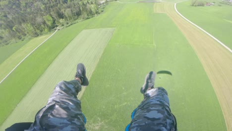 feet of a paraglider in flight over the vast green field in switzerland on a sunny day - pov - aerial