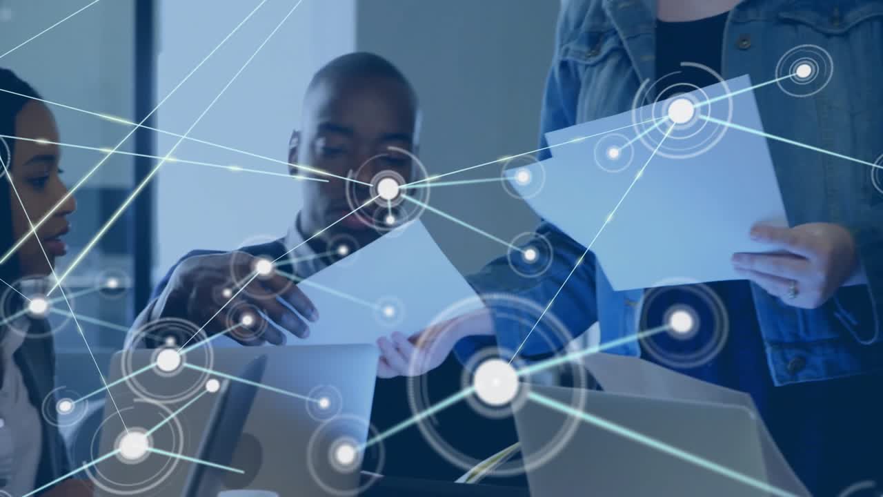 Three professionals reviewing documents on laptops in business meeting with glowing network overlay