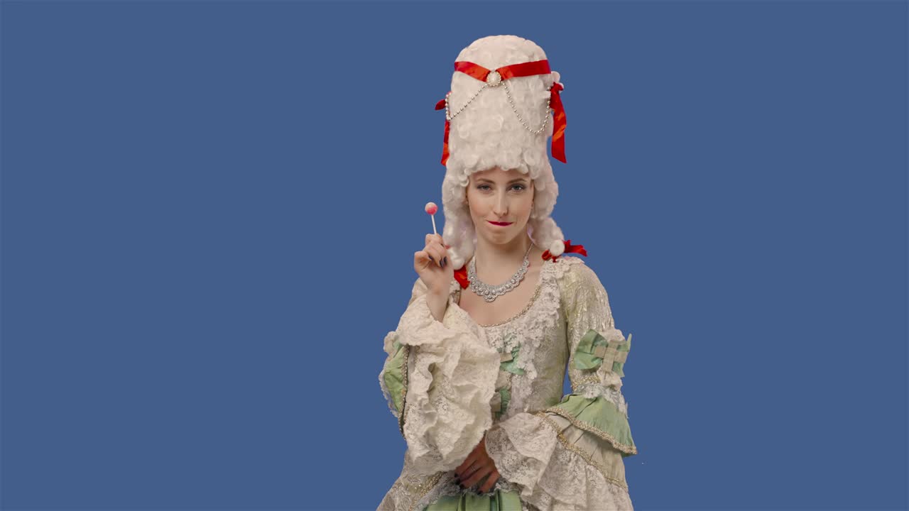 retrato de una dama de la corte con un vestido blanco de encaje vintage y una peluca, disfrutando de una piruleta de caramelo dulce. mujer joven posando en el estudio con fondo de pantalla azul. primer plano. cámara lenta lista 59.94fps