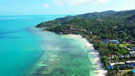 Paradise-white-sandy-exotic-beach-with-vacations-resorts-on-shore-of-tropical-island-washed-by-calm-clear-turquoise-lagoon-in-Thailand