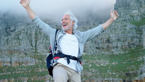 senior man standing with arms up on a rock at countryside 4k