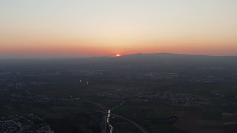 Vista-Aérea-Del-Paisaje-Plano-Por-La-Noche.-Puesta-De-Sol-Detrás-Del-Horizonte.-Vista-Desde-Un-Dron-Volando-Sobre-Un-Pequeño-Pueblo.-Colorido-Cielo-Crepuscular.