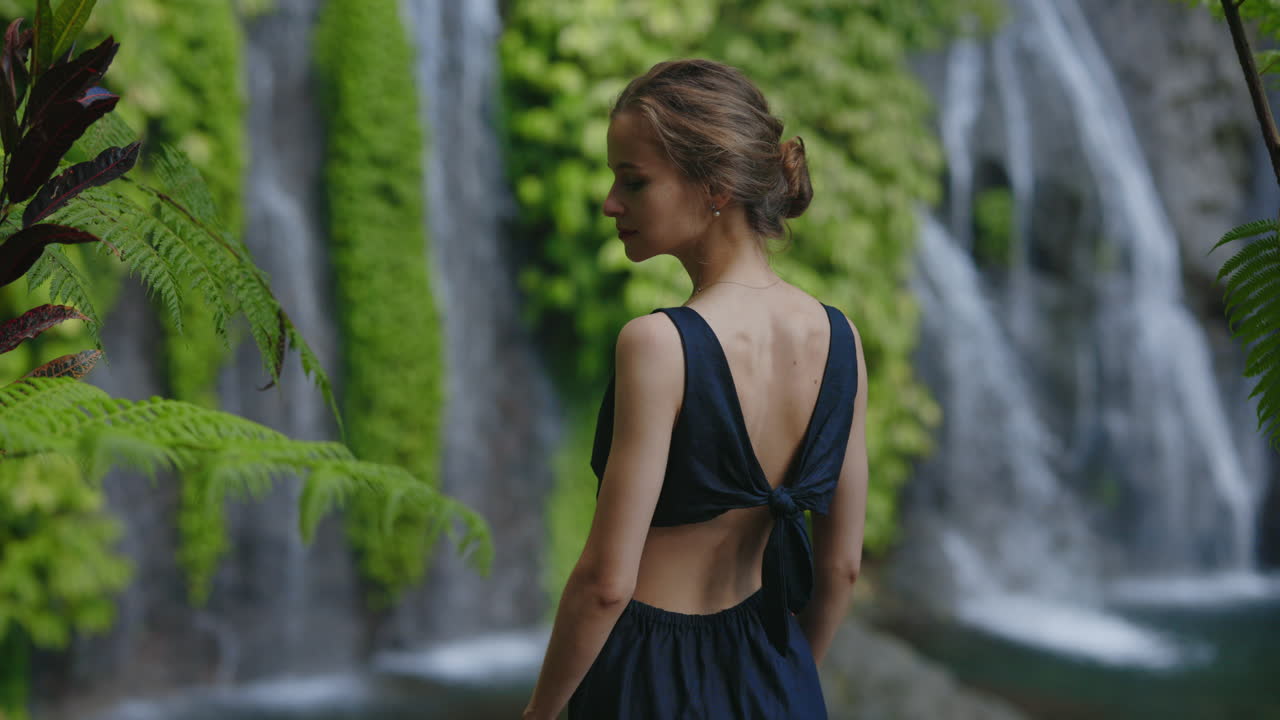 Young Woman Standing Peacefully in Front of a Tropical Waterfall