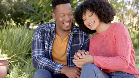 portrait of happy african american couple crouching in garden at home, slow motion