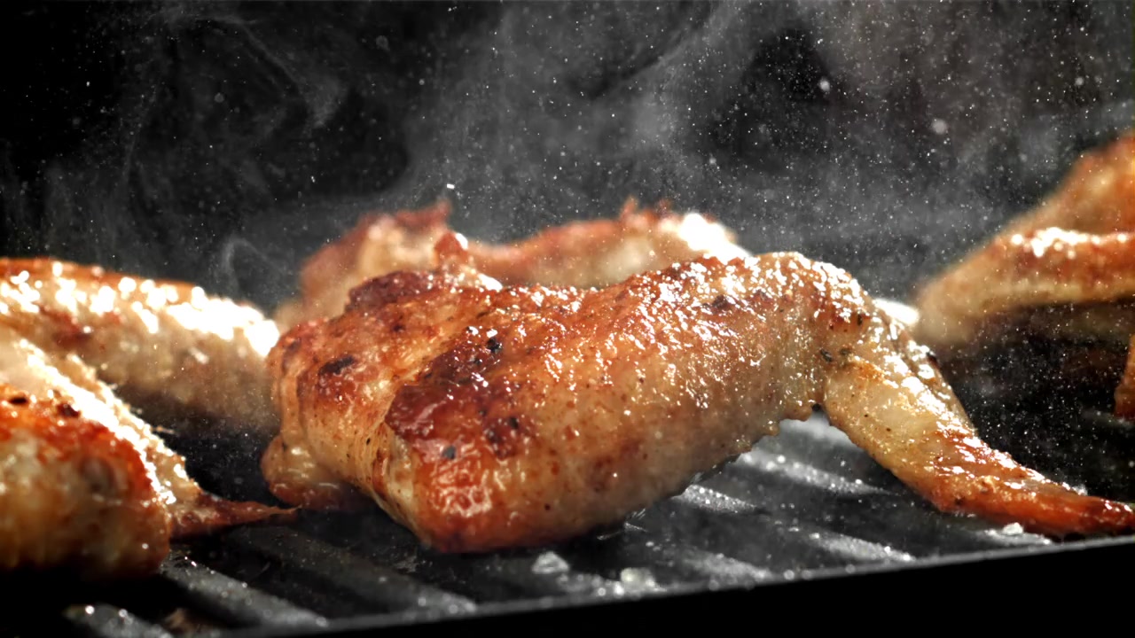 Primo piano di ali di pollo dorate che sfrigolano sulla griglia del barbecue