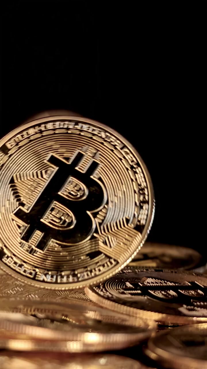 Um token de criptomoeda dourado cai sobre uma pilha de moedas, com iluminação dramática e fundo preto.