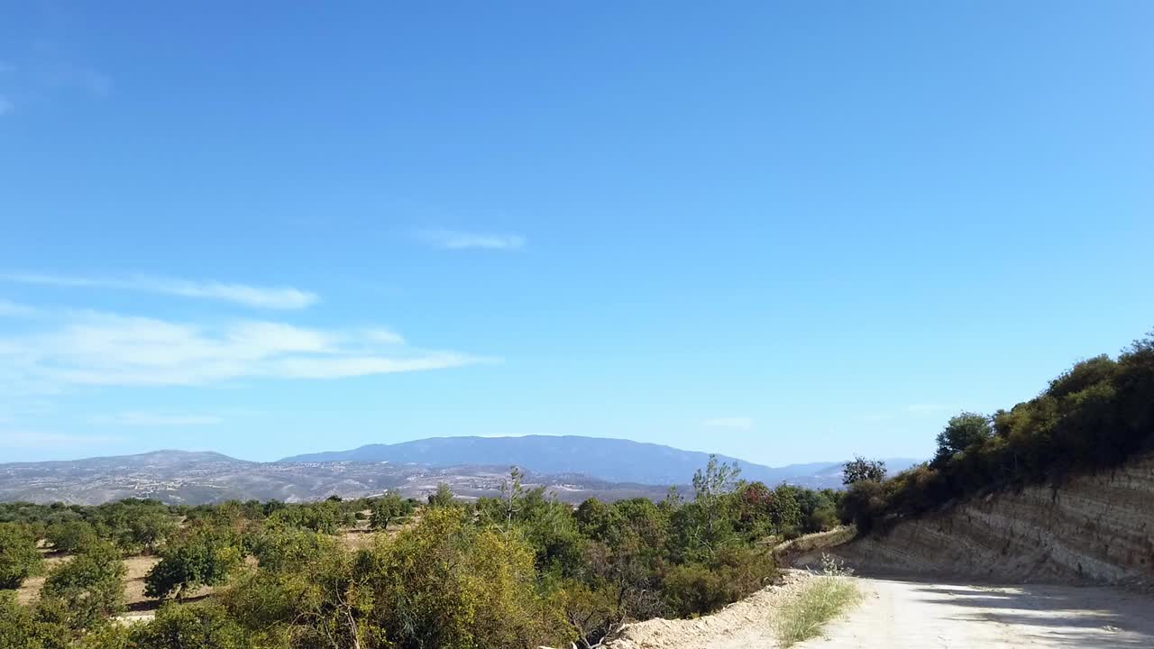 A dirt path leads into the Cyprus countryside, framed by distant mountains and vivid blue skies. This scenic view captures the island’s natural beauty and peaceful rural charm.