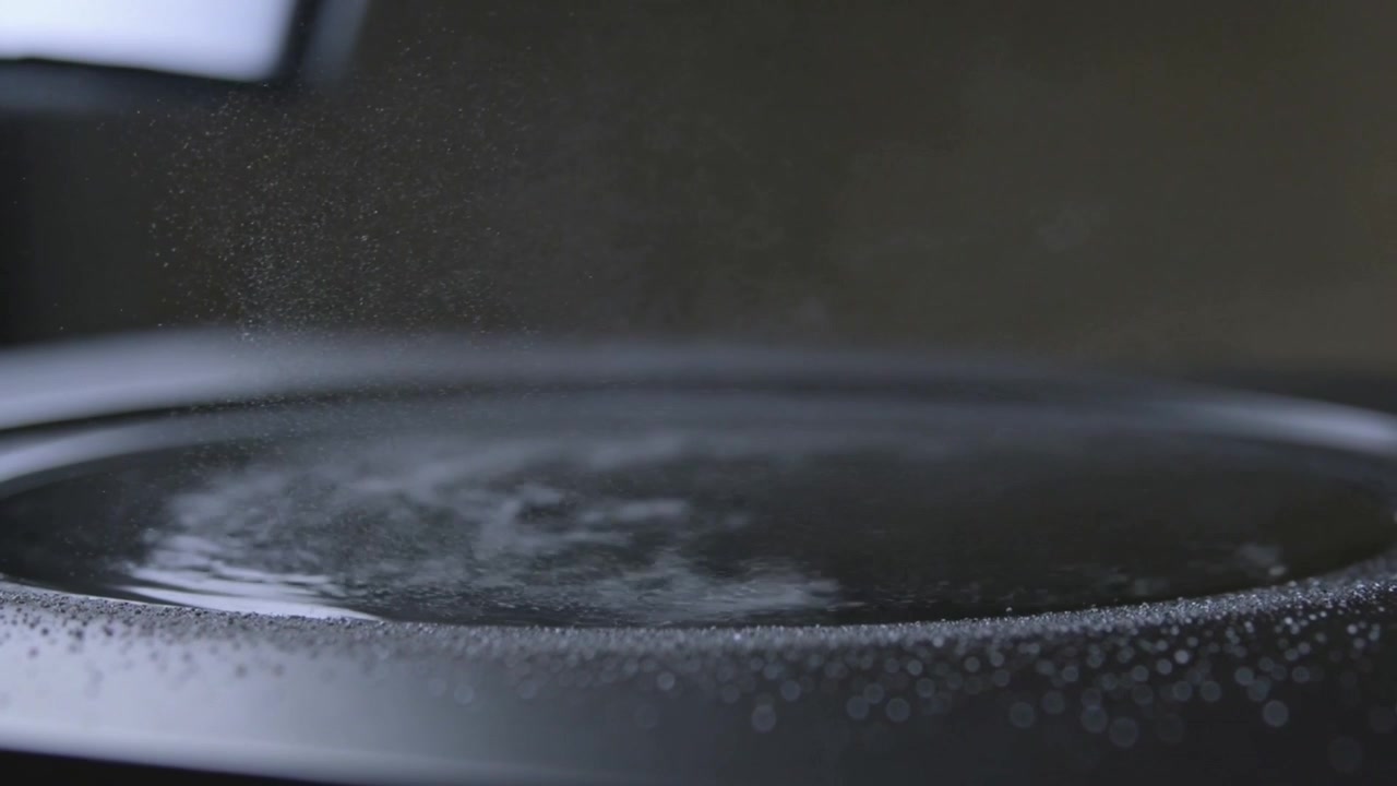 Showing shallow bowl with dark liquid swirling on countertop from subtle motion