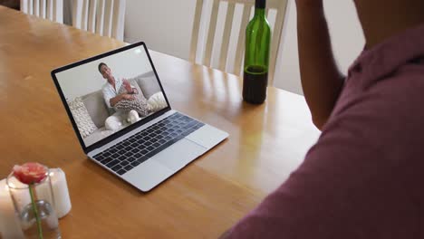 Mid-section-of-african-american-man-drinking-wine-while-having-a-video-call-on-laptop-at-home